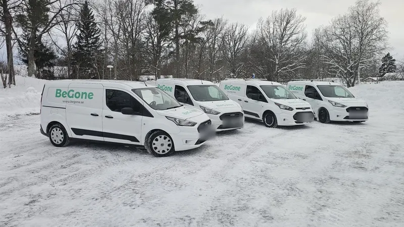 Fyra vita servicebilar med Begones logotyp parkerade på rad i snön