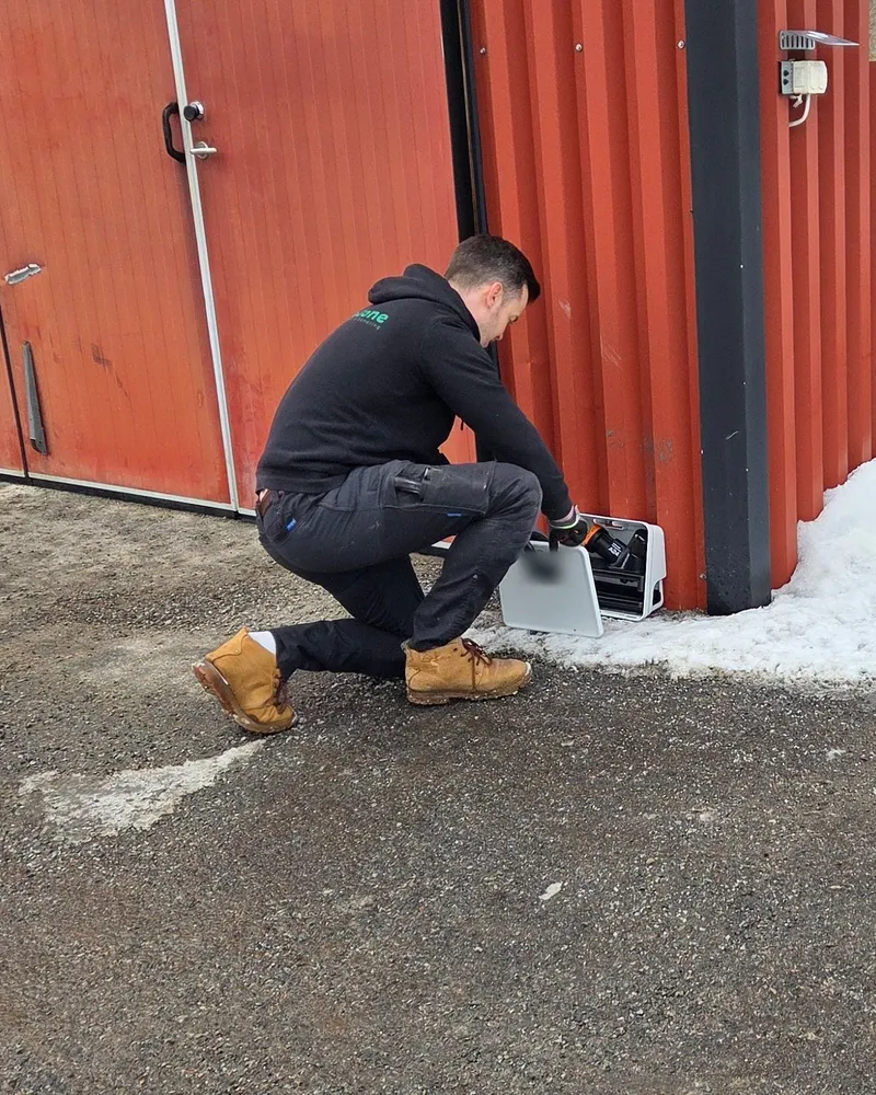 Begones tekniker på knä vid en port, vid en mekanisk råttfälla längs fasaden