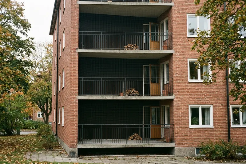 Balkonger på ett flerbostadshus i tegel där varje balkong är inklädd med ett tunt, nästan osynligt fågelnät från räcket upp till balkongplattan ovanför